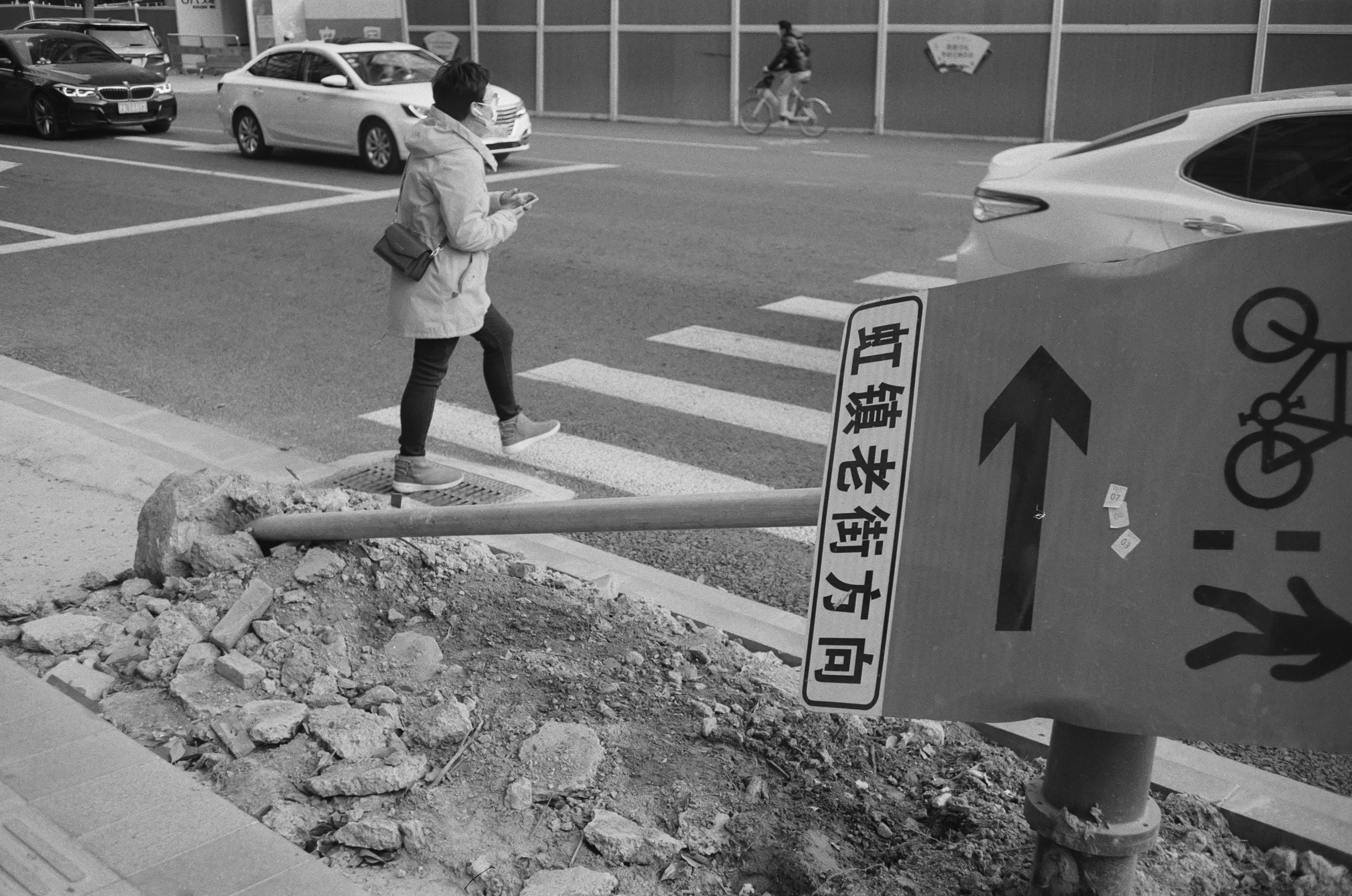 grayscale photo of woman in white jacket and black pants standing on concrete pavement